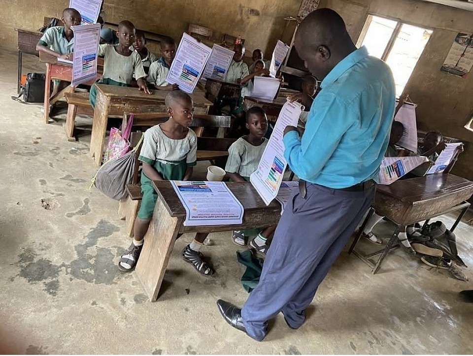 A school teacher, trained by ERWAP Energy Initiative, teaches students about climate change using ERWAP infographics and distributes educational materials to support learning.